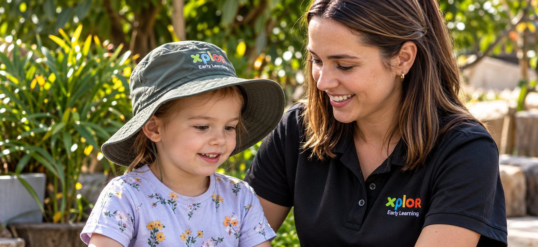 An educator smiling with a child wearing an Xplor sun hat in the garden at Xplor Coomera