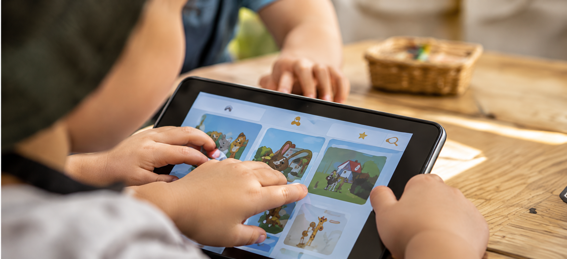 A child tapping the screen of a tablet showing a picture library, guided by an educator at a timber table